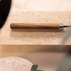 The walnut handle and its stainless ferrule, resting on stone