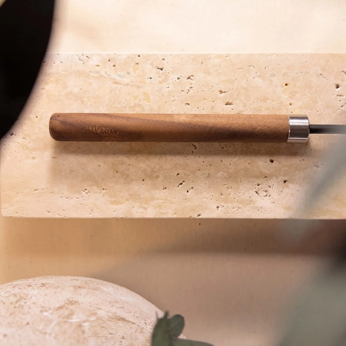 The walnut handle and its stainless ferrule, resting on stone